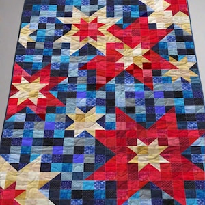 May include: A colorful quilt with a star pattern. The quilt features red, white, and blue stars against a background of blue and navy squares. The quilt is a patchwork design, with each square and star made of different fabrics.