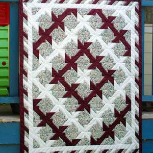 May include: A handmade quilt with a repeating pattern of burgundy crosses and floral-patterned squares on a white background. The quilt has a burgundy border and a white inner border. The quilt is approximately 40 inches wide and 50 inches long.
