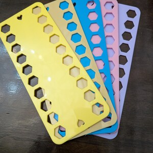 May include: A collection of plastic thread organisers in shades of yellow, beige, blue, pink, and lilac. Each organiser features a pattern of hexagonal cutouts and a heart-shaped hole. These are designed for organising embroidery floss or thread.