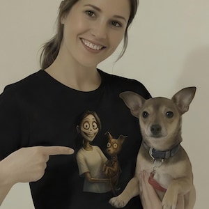 May include: Black t-shirt with a cartoon illustration of a character and a cat. The person in the image is pointing at the graphic. A small dog with a leash is being held.
