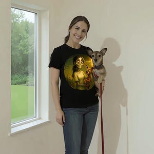 May include: Black t-shirt with a circular cartoon graphic of a character holding a doll. The person in the image is wearing blue jeans and holding a small dog on a leash. The background is a plain white wall with a window.