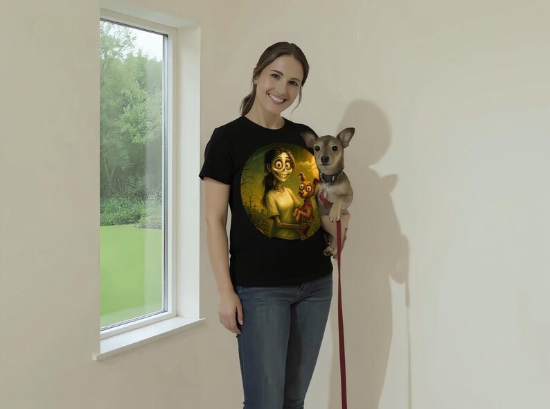 May include: Black t-shirt with a circular cartoon graphic of a character holding a doll. The person in the image is wearing blue jeans and holding a small dog on a leash. The background is a plain white wall with a window.