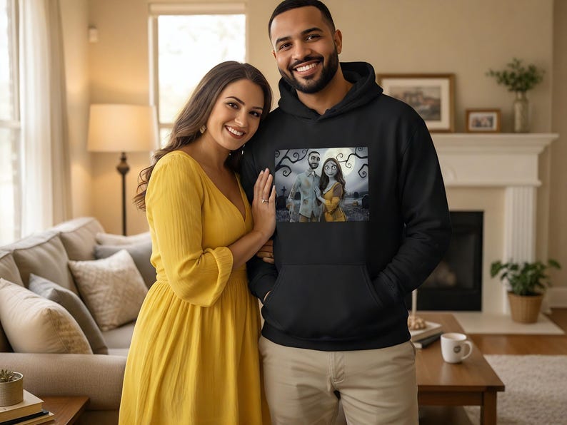 Peut inclure: Un sweat &agrave; capuche noir avec une impression graphique d'un couple dans un cadre effrayant. Une femme en robe jaune se tient &agrave; c&ocirc;t&eacute; d'un homme portant le sweat-shirt. La femme porte une robe jaune. L'arri&egrave;re-plan comprend un canap&eacute;, une lampe et une chemin&eacute;e.
