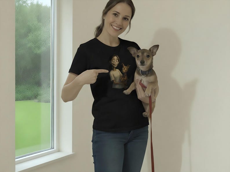 May include: Black t-shirt with a cartoon illustration of a character and a cat. The person in the image is pointing at the graphic. A small dog with a leash is being held.