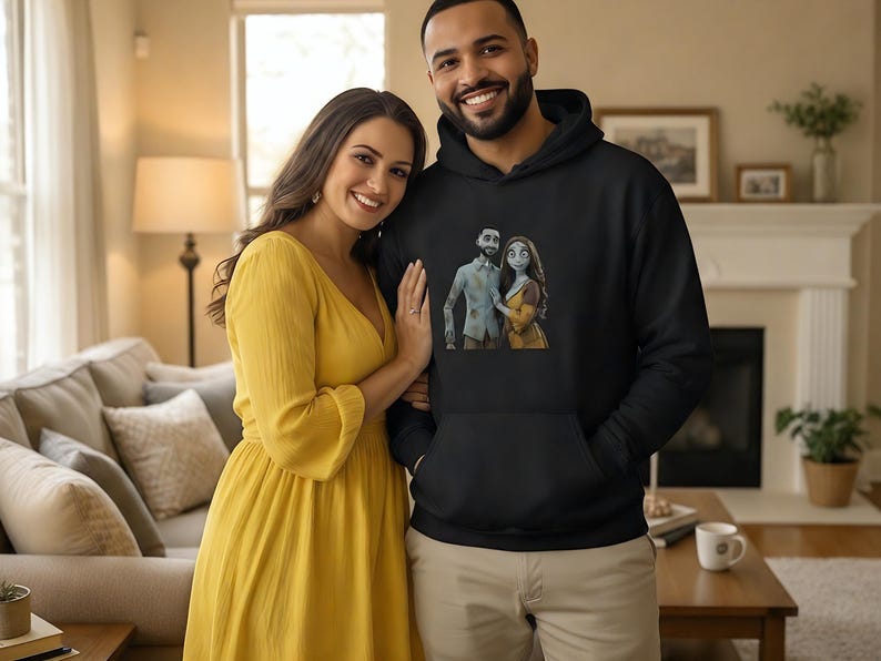 Peut inclure: Un sweat &agrave; capuche noir avec un motif de couple de dessins anim&eacute;s. Une femme en robe jaune et un homme en sweat &agrave; capuche noir sourient. L'arri&egrave;re-plan comprend un salon avec un canap&eacute;, une chemin&eacute;e et une table.