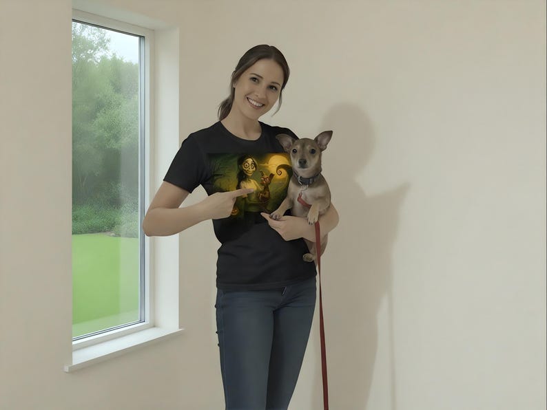 May include: Black t-shirt with a graphic design featuring a character with a yellow light and a swirling background. The person is holding a small brown dog with a leash. The person is pointing at the graphic on the shirt.