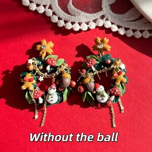 May include: A pair of festive earrings featuring miniature Christmas wreath designs. Each wreath includes a gingerbread man, snowman, mushrooms, and acorns, with gold chain accents and a flower at the top. The text "Without the ball" is at the bottom.