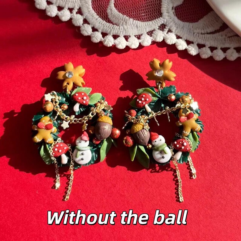 May include: A pair of festive earrings featuring miniature Christmas wreath designs. Each wreath includes a gingerbread man, snowman, mushrooms, and acorns, with gold chain accents and a flower at the top. The text "Without the ball" is at the bottom.