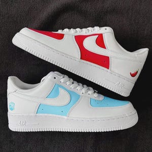 May include: Two pairs of white sneakers with colorful accents. One pair features red and white panels with a red chili pepper graphic. The other pair has light blue and white panels with a blue cube graphic.