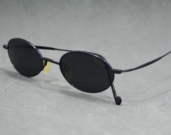 May include: Oval-shaped sunglasses with dark lenses and a thin, dark blue frame. The sunglasses have a classic design with a sleek, minimalist aesthetic. The temples curve gently to the ear pieces.