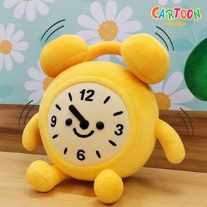 May include: A yellow plush alarm clock with a smiling face, black hands, and the numbers 12, 3, 6, and 9. The clock has two yellow bells on top and the text "CARTOON plushies" in the upper right corner.