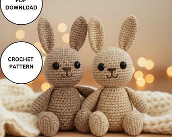 May include: Two crocheted bunny dolls in a light brown color. The bunnies have large black eyes, long ears, and are sitting on a white blanket. The image includes text that says "PDF DOWNLOAD" and "CROCHET PATTERN".