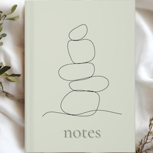 May include: A notebook with a light green cover featuring a minimalist line drawing of stacked stones. The word "notes" is printed in a subtle, gray font at the bottom. The design evokes a sense of calm and simplicity.