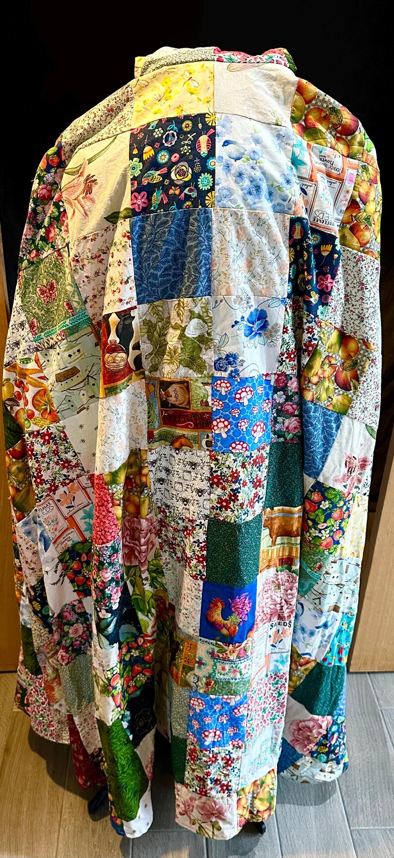 May include: A patchwork quilt coat featuring a variety of floral, fruit, and rooster patterns. The coat is made of numerous fabric squares in various colors, including red, blue, green, and yellow. The coat is a unique piece of wearable art.