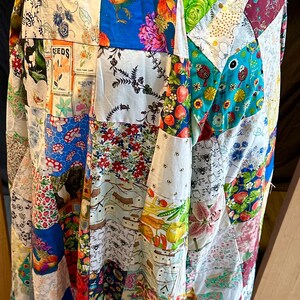 May include: A patchwork coat with a variety of fabric patterns, including floral, rooster, and botanical prints. The coat has a blue hood and a red flower closure. The coat is made of various fabric squares sewn together.