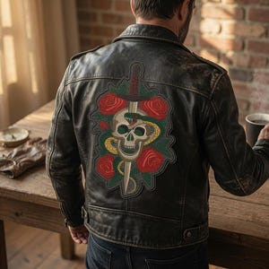 May include: A black leather jacket featuring a large embroidered patch on the back. The patch displays a central skull pierced by a dagger, surrounded by a coiled green snake and several red roses with dark green leaves, all set against a black background.
