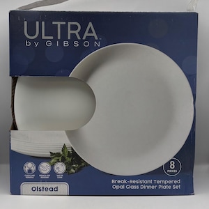 May include: A boxed set of eight white opal glass dinner plates. The box is dark blue with the brand name "ULTRA by GIBSON" and the product name "Olstead". The box also states the plates are break-resistant and easy to clean.