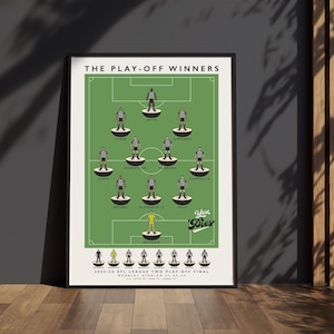 以下が含まれることがあります： 緑色のサッカー場デザインと「THE PLAY-OFF WINNERS」の文字が入った額入りのポスター。ポスターには、選手名と「2023/24 EFL LEAGUE TWO PLAY-OFF FINAL」の文字が記載されたチームのラインナップが掲載されています。ポスターは黒いフレームに入っています。