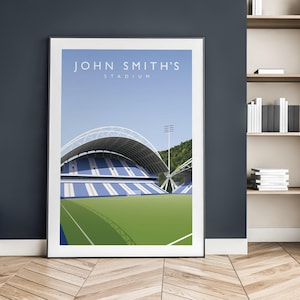 Könnte beinhalten: Ein gerahmter Kunstdruck mit dem John Smith's Stadium. Das Stadion hat blau-weiß gestreifte Sitzplätze, einen grünen Rasen und ein geschwungenes Dach. Der Himmel ist hellblau. Der Druck wird an einer Wand mit Holzboden gezeigt.