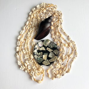 May include: A white shell necklace with a brown seashell and a black and white shell dish with the word "HAWAII" on it.