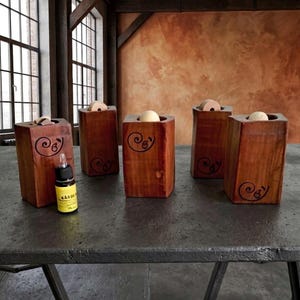 Può includere: Cinque blocchi di legno rettangolari con finitura liscia, ciascuno dotato di un foro circolare sulla parte superiore contenente una sfera chiara e un grafico a spirale nera sul davanti. Un piccolo flacone giallo con tappo è in primo piano.