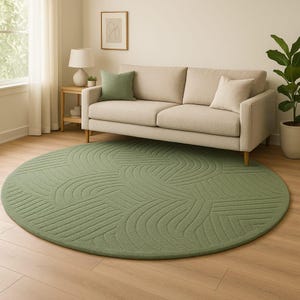 May include: A circular, sage green rug with a geometric design is the focal point. It sits on a wooden floor, with a beige sofa and green cushions behind it. A lamp and framed art are also in the room.