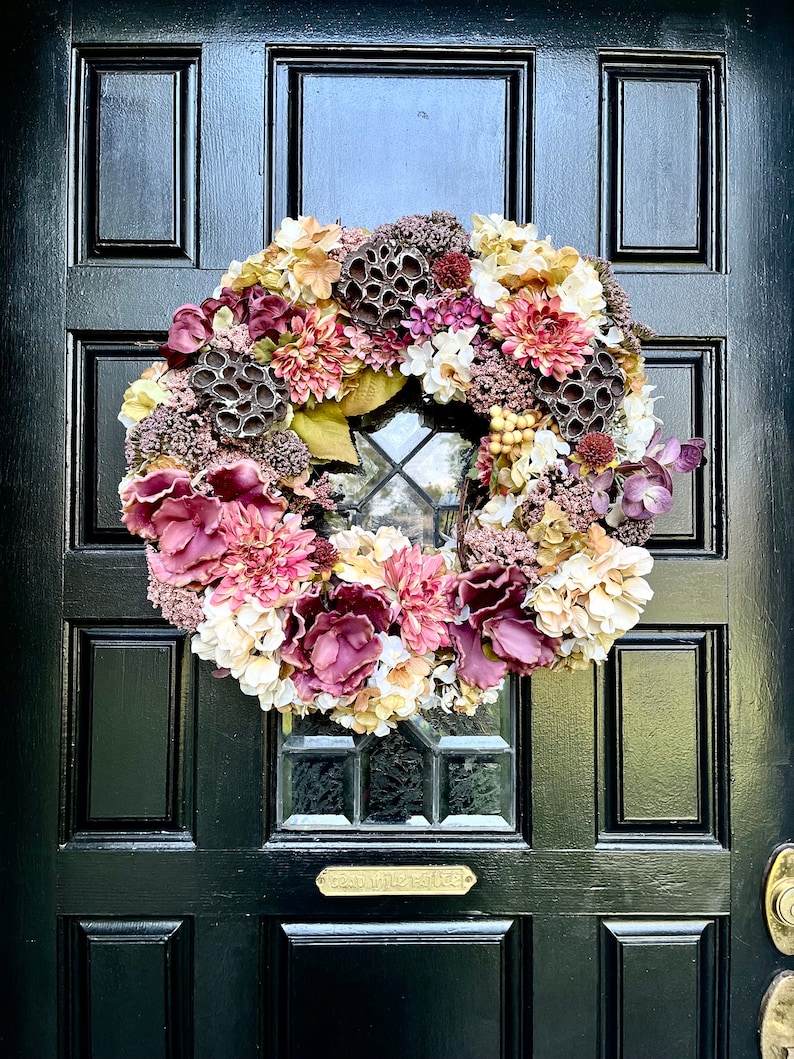 May include: A wreath with burgundy, cream, and gold flowers and dried seed pods hanging on a black door with a brass door knocker and a brass plaque that reads 'Country Estate'.