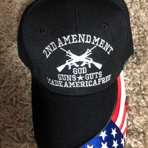 May include: Black baseball cap with a white embroidered design that says "2nd Amendment God Guns Guts Made America Free" and a red, white, and blue American flag design on the brim.