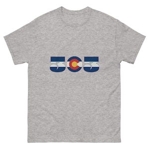 May include: A heather gray t-shirt featuring the number "505" in a stylized design. The design incorporates the Colorado state flag colors: blue, white, red, and yellow. The shirt is made of a soft, comfortable material.