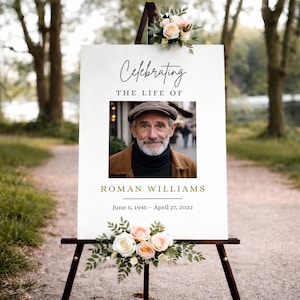 Puede incluir: Un letrero conmemorativo blanco sobre un caballete de madera, adornado con arreglos florales. El letrero dice "Celebrando la vida de Roman Williams" con una foto de un hombre. También se muestran las fechas 5 de junio de 1945 – 27 de abril de 2022.