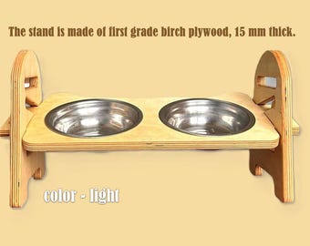 May include: A light-colored, wooden pet feeder with two stainless steel bowls. The stand is made of birch plywood, 15 mm thick. The text "color - light" is visible.