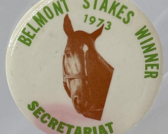 May include: A round, white button with green text that reads "Belmont Stakes 1973 Winner" and "Secretariat." The button features a brown horse head silhouette.