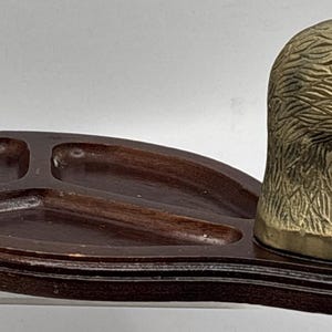 May include: A dark brown wooden tray featuring three recessed compartments and a polished brass duck head attached to one end. The tray has a smooth, varnished finish, and the brass duck head displays detailed feather textures and a smooth beak.