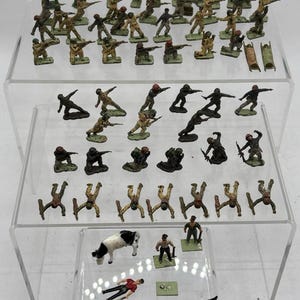 May include: A collection of vintage toy soldiers in various poses, including soldiers with rifles, lying down, and standing. The figures are painted in shades of green, brown, and tan. Also included are toy horses, a cow, and a small stretcher.
