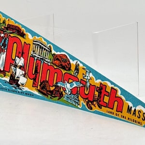 May include: A triangular felt pennant featuring the text Plymouth Mass Land of the Pilgrims. The design includes illustrations of a ship, historical figures, a building, and a lobster against a blue background with yellow accents and two yellow ties.