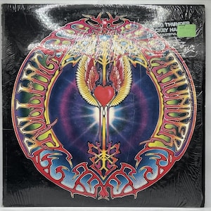 May include: A square vinyl record cover featuring a circular graphic with a central red heart and yellow wings. The text Rolling Thunder is written in stylized lettering around the circle. The background is a dark blue and purple gradient.
