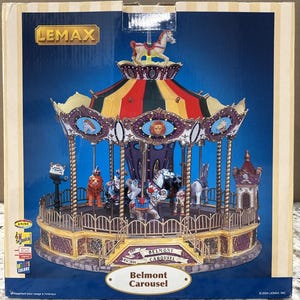 May include: A Lemax Belmont Carousel miniature display featuring a multi-colored striped roof, ornate purple and gold detailing, and various animal figures including horses, lions, and elephants. The base is labeled The Belmont Carousel Est. 1893.