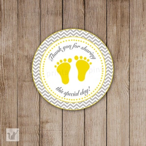 May include: Round gray and yellow baby shower favor sticker with a chevron pattern. The sticker says "Thank you for sharing this special day!" and has two yellow footprints.