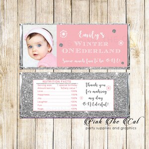 May include: A pink and silver chocolate bar wrapper with a photo of a baby girl. The wrapper says "Emily's Winter Wonderland" and "Snow much fun to be one!"  The back of the wrapper has a nutrition facts label and says "Thank you for making my day ONEderful!"  Pink The Cal party supplies and graphics.