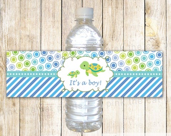 May include: Water bottle label with a blue and green striped background. The label features a green and blue turtle with the text "It's a boy!" in a white cloud.