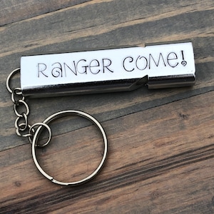 May include: A silver whistle with a keychain attached. The whistle has the words "Ranger Come!" engraved on it.