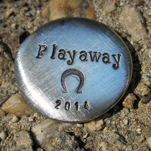 May include: A silver disc with the words "Playaway" and the year "2014" engraved on it. The disc also features an omega symbol.