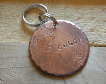 May include: Copper dog tag with a paw print design and the name "CHLOE" engraved on it. The tag is attached to a silver key ring.