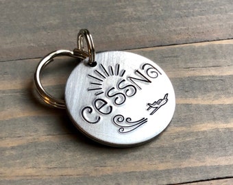 May include: Silver keychain with a round tag that says "Cessna" with a small airplane and a sunburst design.