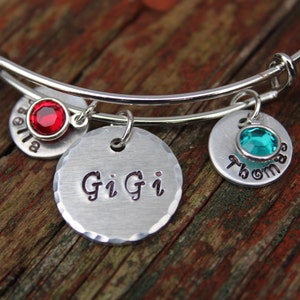 May include: A silver charm bracelet with three charms. The charms are engraved with the names "Bella", "Gigi", and "Thomas". The charms are decorated with red and turquoise gemstones.