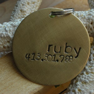 May include: Brass dog tag with the name "ruby" and the phone number "413.301.788" engraved on it.
