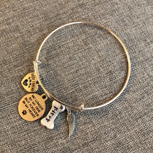 Op de afbeelding: Zilveren armband met bedels. De bedels zijn een hart met poot afdrukken waarop "Beste vriend" staat, een ronde bedel waarop "Niet langer aan mijn zijde, maar voor altijd in mijn hart" staat met een poot afdruk, een bot bedel met het nummer "414" erop en een zilveren engelenvleugel bedel.