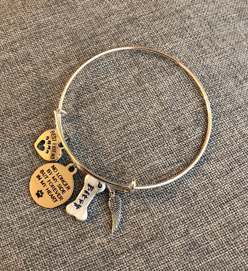 Op de afbeelding: Zilveren armband met bedels. De bedels zijn een hart met poot afdrukken waarop "Beste vriend" staat, een ronde bedel waarop "Niet langer aan mijn zijde, maar voor altijd in mijn hart" staat met een poot afdruk, een bot bedel met het nummer "414" erop en een zilveren engelenvleugel bedel.