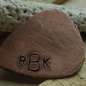 May include: A copper guitar pick with the initials "RBK" engraved on the front.
