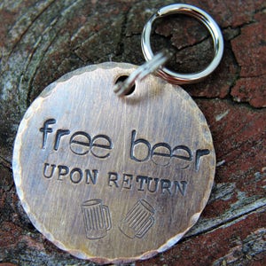 May include: A round, brass-colored tag with the words "free beer upon return" engraved on it. The tag is attached to a silver key ring.